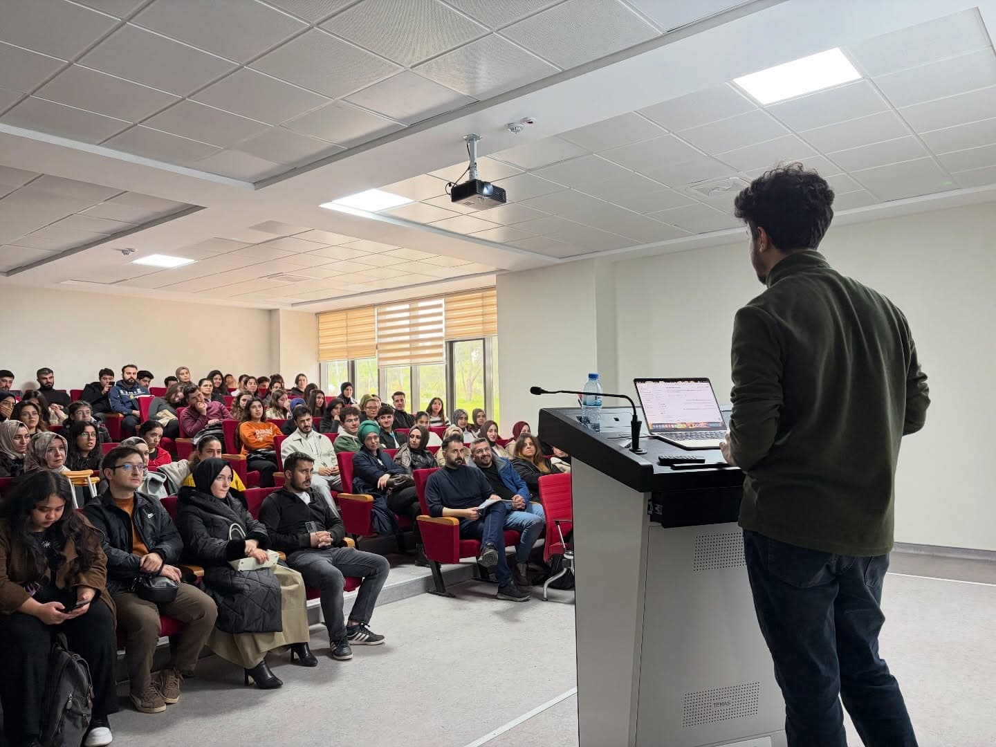 Seminer salonunda kürsüden dinleyicilere hitap eden konuşmacı
